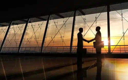 two people in an open office space shaking hands silhouetted by a sunset