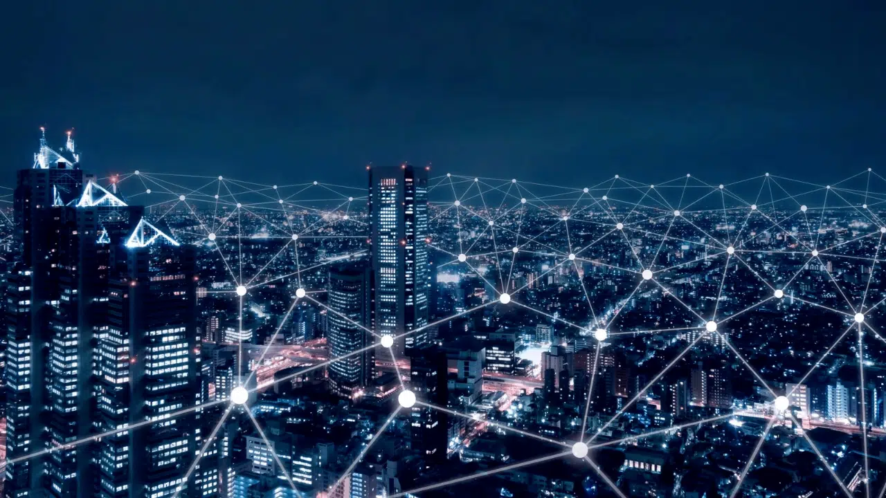 Night city skyline with glowing interconnected nodes and lines representing a smart city network in the night sky versus the urban landscape after dark, conveying IoT connectivity across buildings.